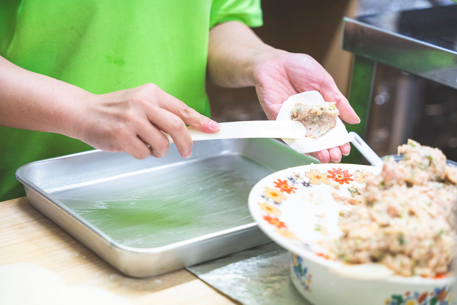 店主的妻子和服務人員熟練地拉伸麵團，並將豆沙包裹穿過玻璃門