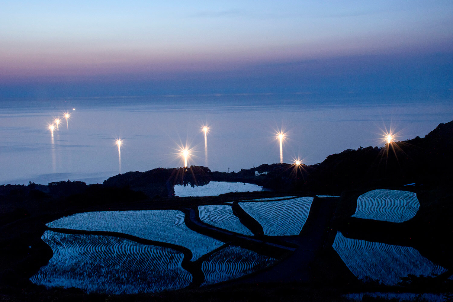 わずかな残照を映し青く浮かび上がる棚田と日本海にゆらめく漁り火を一緒に眺められる
